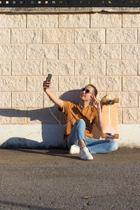 Young man taking a selfie photo with skateboard to send to friends while sitting on the floor