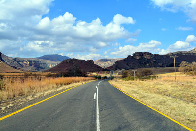 Road amidst field by mountains against sky