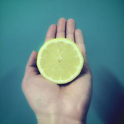 Close-up of hand holding lemon slice over colored background