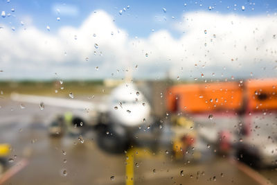 Raindrops on glass window against airplane at airport runway