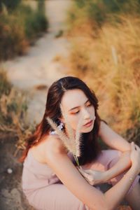 High angle view of young woman holding plant while sitting at field on sunny day