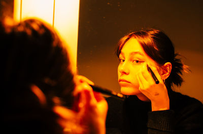 Close-up of young woman applying eyeliner while reflecting on mirror