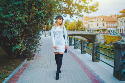 Young woman walking on footpath by railing against tree