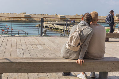 Rear view of people sitting on pier against sky