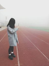 Full length of woman standing on running tracks during foggy weather