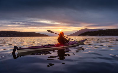 Man and woman on boat against sky during sunset