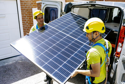 Engineers wearing hardhat carrying solar panel on sunny day