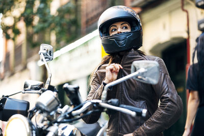 Biker woman in helmet wearing leather jacket while looking away in city