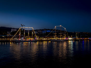 Illuminated city by river against sky at night