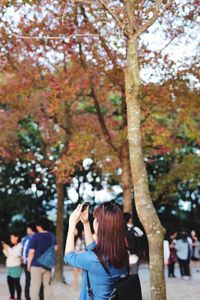 Woman photographing autumn trees in park