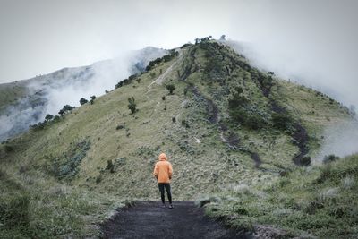 Rear view of man walking on road against mountain range