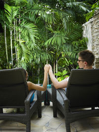 Couple holding hands while relaxing on lounge chairs at poolside