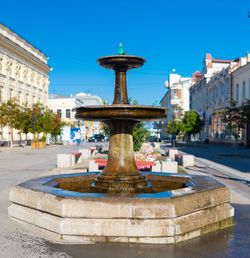 Fountain in city against clear blue sky