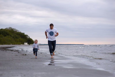 Father and daughter playing at beach against sky