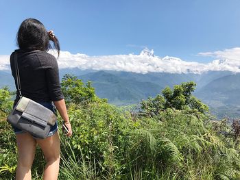 Rear view of woman standing on mountain against sky during sunny day