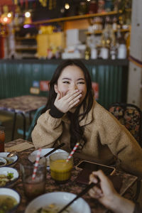 Woman laughing while covering mouth at restaurant