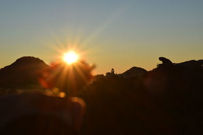 Sun shining over silhouette land against sky during sunset
