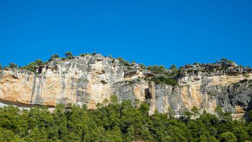 Low angle view of rocks against clear blue sky