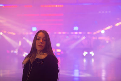 Portrait of woman standing against illuminated light at night