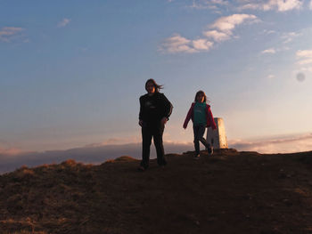 Siblings walking on mountain against sky during sunset