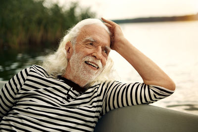 Portrait of content senior man with white hair and beard sitting in rowing boat on a lake