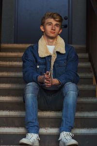 Full length of thoughtful young man looking away while sitting on staircase