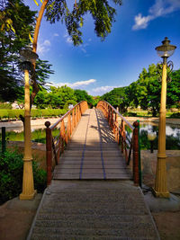 Empty footpath bridge amidst trees against sky