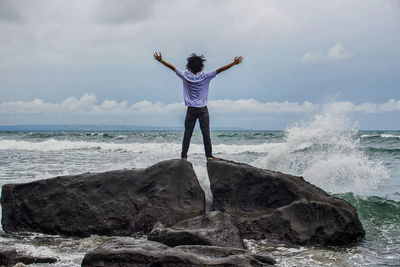 Rear view of man standing on rocks in sea