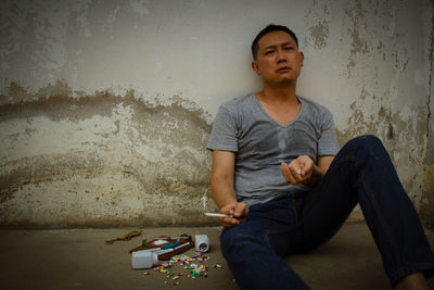 Man smoking marijuana joint while sitting against wall