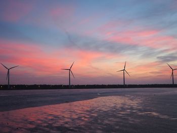 Wind turbines on field against sky at sunset