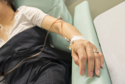 Cropped hand of woman with iv drip on bed in hospital