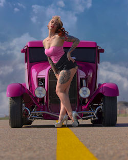 Young woman, pinup model with tattoos posing in front of hot pink vintage car