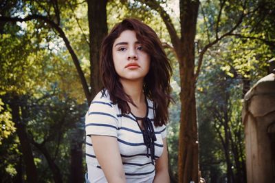 Portrait of beautiful young woman standing against tree trunk