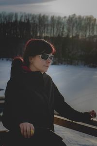 Woman wearing sunglasses while standing by railing on snow