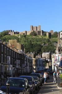 Cars on road by buildings against clear blue sky