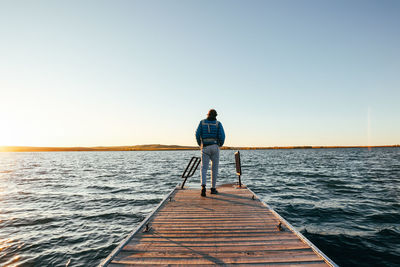 Rear view of man walking on pier over sea against clear sky