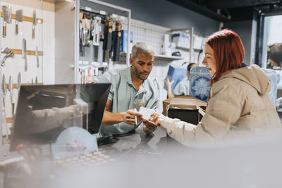 Male retail clerk showing bill to female customer at checkout in electronics store