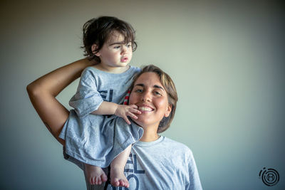 Happy mother and daughter standing against wall