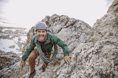 Male rock climber with rope and helmet sticks tongue out