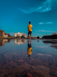 Rear view of man standing by lake against sky