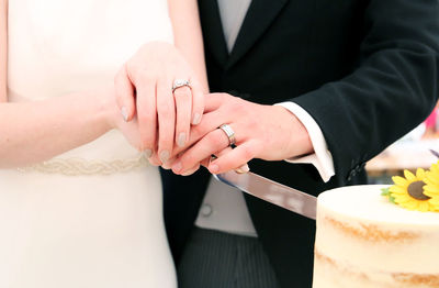 Midsection of bride and groom cutting cake with knife