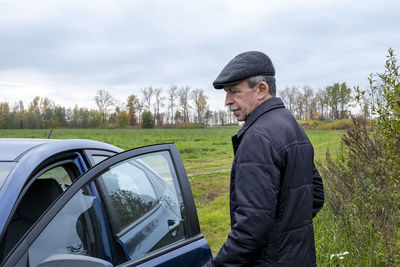 Man standing by car on road against sky