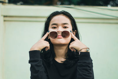 Portrait of young woman wearing sunglasses against wall