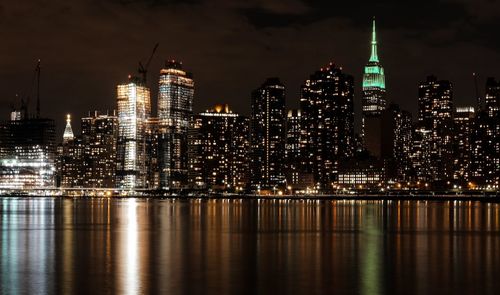 Illuminated empire state building by east river against sky in manhattan at night