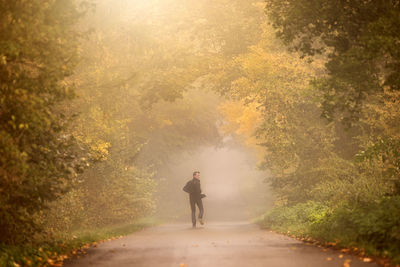 Rear view of man on road amidst trees during autumn