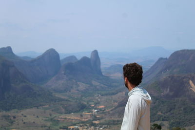 Rear view of man standing on mountain against sky
