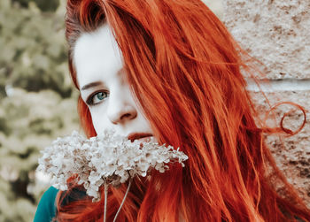 Portrait of beautiful woman holding flower standing by wall outdoors