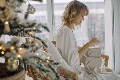 Woman looking at packages while sitting by christmas tree at home