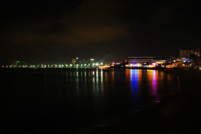 Illuminated buildings by river against sky at night