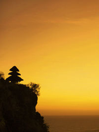 Silhouette temple by sea against sky during sunset at uluwatu , bali